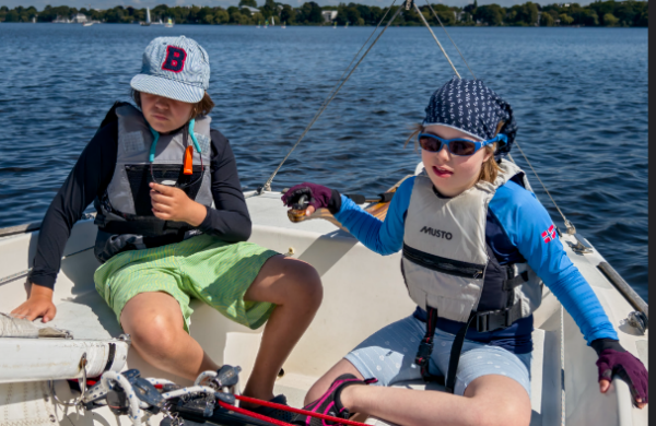 Zwei Kinder sitzen in einem Segelboot auf dem Wasser und lernen Segeln.